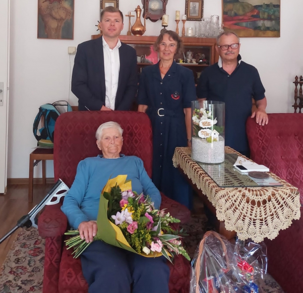 Spotkanie z okazji 100 urodzin Lidii Więckowskiej, kombatantki, żołnierki Armii Krajowej. Zdjecie wykonane w mieszkaniu jubilatki. Pani Lidia siedzi w fotelu. Obok niej stoi wicedyrektor Gabinetu Marszałka - Marcin Kordela, a także kobieta i mężczyzna.