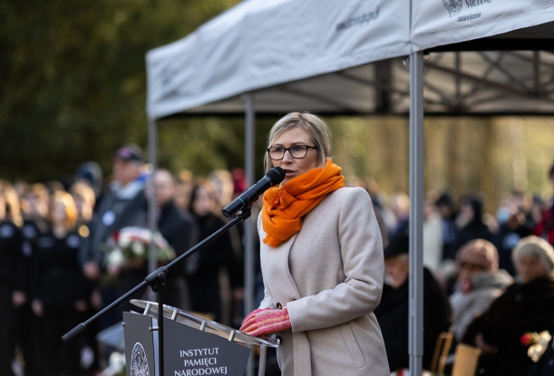 Kobieta przemawiająca do mikrofonu podczas plenerowej uroczystości.