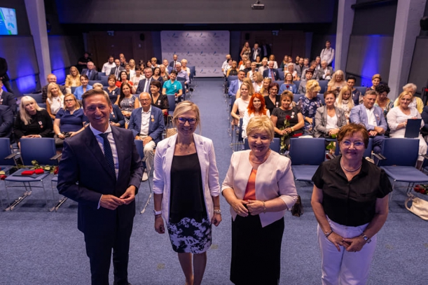 Wszyscy uczestnicy gali wręczenia odznak na tle sali. 