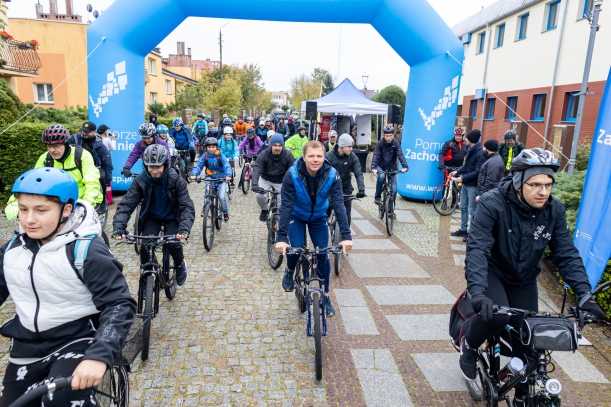 Rowerzyści na starcie rajdu, w tle grupa cyklistów, brama promocyjna Pomorza Zachodniego.