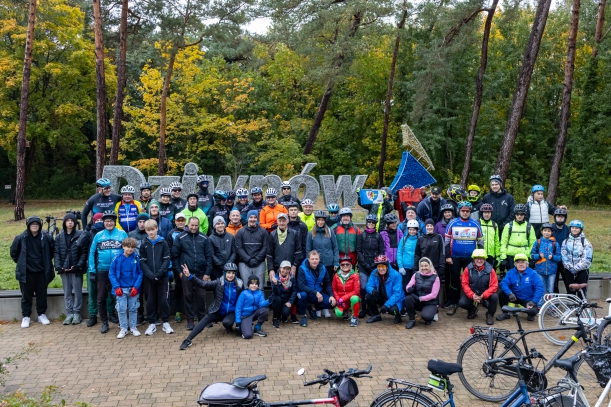 Uczestnicy rajdu podczas współnego zdjęcia, w tle zieleń i napis Dziwnów. 
