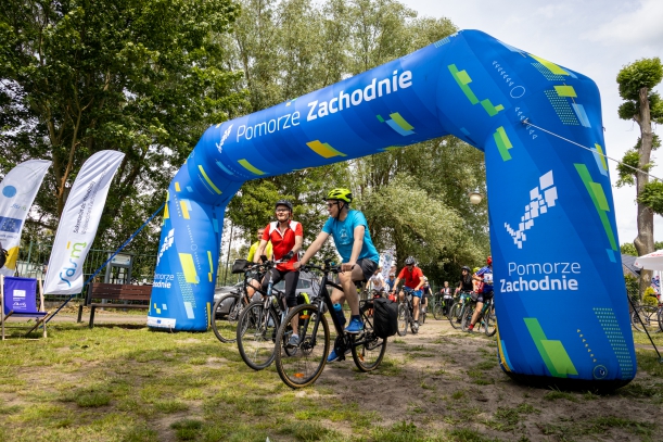 Meta rajdu z uczestnikami, w tle stoiska promocyjne i teren zielony. 