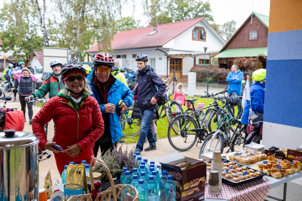 Punkt regeneracyjny z ciepłuymi napojami, na pierwzym planie stoły z poczęstunkiem, w tle rowerzyści. 