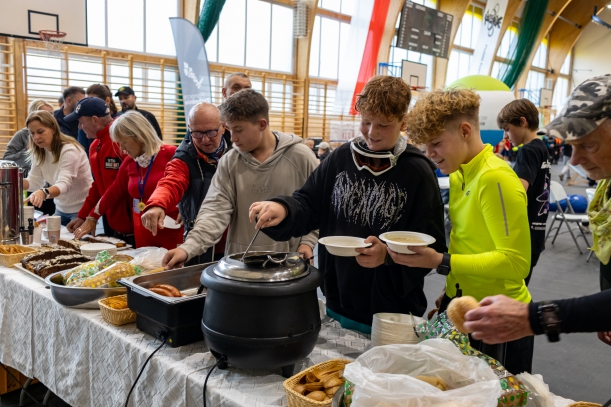 Goracy posiłek po rajdzie, przy stołach rowerzyści, w tle hala sportowa. 