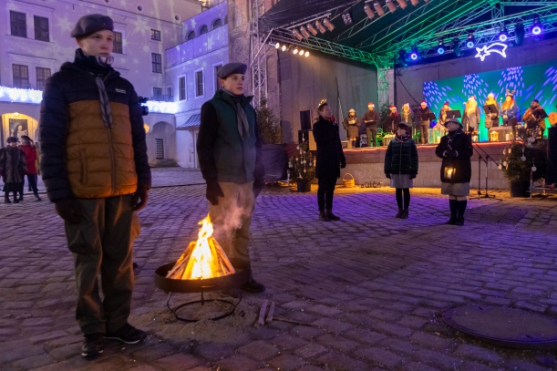 Uroczystość przekazania Betlejemskiego Światła Pokoju przez harcerzy Zachodniopomorskiej Chorągwi ZHP marszałkowi Olgierdowi Geblewiczowi i mieszkańcom Pomorza Zachodniego. Na pierwszym planie - dwaj harcerze stoją przy ognisku. W tle - oświetlona scena.