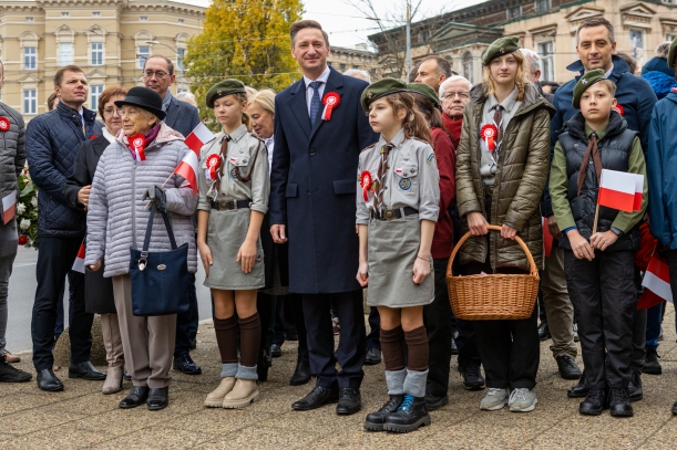 Uroczystość z okazji Narodowego Święta Niepodległości przy pomniku marszałka Józefa Piłsudskiego w Szczecinie. Około 30 osób stoi na chodniku z biało-czerwonymi chorągiewkami. Wśród nich marszałek województwa Olgierd Geblewicz, obok niego harcerze.