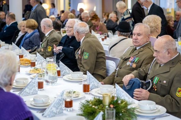 Wigilia dla kombatnatów zorganizowana przez Urząd Marszałkowski Województwa Zachodniopomorskiego w Zakładzie Aktywności Zawodowej w Dobrej. Przy stołach siedzi kilkadziesiat osób. Na pierwszym planie - grupa starszych mężczyzn w wojskowych mundurach.