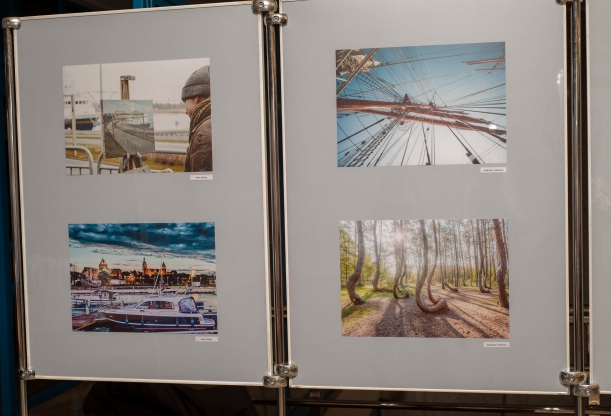 Wernisaż wystawy "Otwarte Pomorze Zachodnie. Oczami Imigrantów" w Książnicy Pomorskiej w Szczecinie. Zbliżenie na dwie tablice zamontowane na stależu. Na tabliach - cztery fotografiie Wałów Chrobrego, żaglowca i tzw. Krzywego Lasu w Nowym Czarnowie.