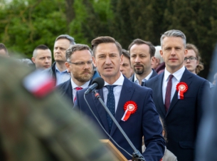 Święto Narodowe Trzeciego Maja - uroczystości przy Pomniku Czynu Polaków. Marszałek Olgierd Geblewicz przemawia do mikrofonu. Obok niego stoją m.in. wojewoda Zbigniew Bogucki i poseł Arkadiusz Marchewka. Za nimi jeszcze kilkanaście osób.