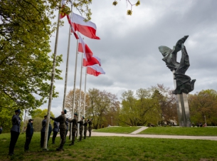 Dzień Flagi Rzeczypospolitej Polskiej. Uroczystości przy Pomniku Czynu Polaków w Szczecinie. Na pięciu masztach łopoczą biało-czerwone flagi. Przy maszatch - żółnierze, obok stoją salutujący policjanci i funkcjonariusze innych służb.